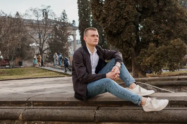 Genç adam düşünceli bir şekilde parktaki bir çıkıntıda oturuyor..