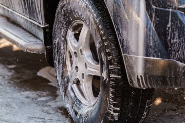 Araba Yıkama esnasında sabun köpüğüyle kaplanmış bir araba tekerleğinin yakın çekim görüntüsü.