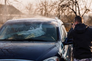 Dışarıda Sunset 'te yüksek basınçlı çamaşır makinesiyle siyah jipi yıkayan adam..