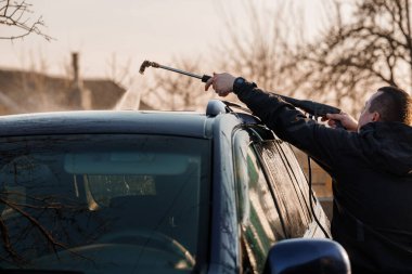 Adam gündüz vakti yüksek basınçlı su püskürterek arabanın çatısını yıkıyor..