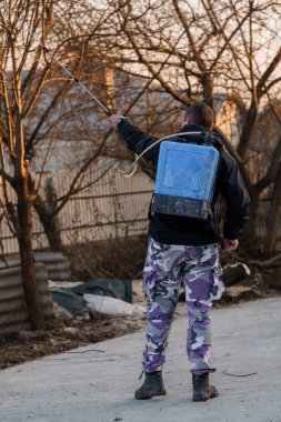 Kamuflaj pantolonlu bir adam Sırt çantalı ağaçlara sprey sıkar Sunset 'te.