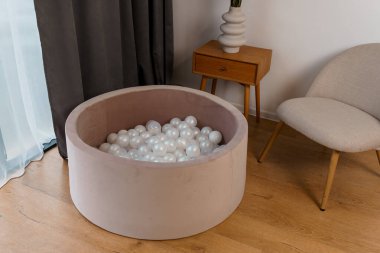 Minimalist Tahta Masa ve Gri Sandalyenin yanı sıra Beyaz Plastik Toplarla dolu Bej Soft Top Çukuru ile Modern Ev İçi.