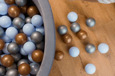 Ahşap zemindeki bir çocuk top havuzunda çok renkli plastik topların yakın görüntüsü.