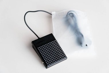 Beyaz yüzeyde Siyah Elektrikli Dikiş Makinesi Ayak Pedalı Kontrolörü ve Şeffaf Plastik Paketleme.