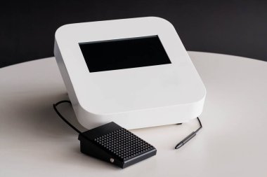 Dokunmatik Ekran, Siyah Ayak Pedalı ve Yuvarlak Masa Üzerinde Stylus Kalemi olan Modern Beyaz Dijital Makine.