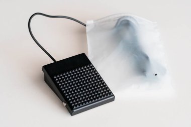 Beyaz yüzeyde Şeffaf Plastik Torbanın İçinde Eklenmiş Kablo ile Siyah Ayak Pedalı Anahtarı.