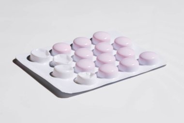 Beyaz yüzeyde zaten kullanılmış tabletlerle dolu yuvarlak soluk pembe haplar paketi..