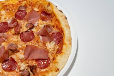 Sucuklu, jambonlu ve beyaz tabakta peynirli leziz İtalyan pizzası..