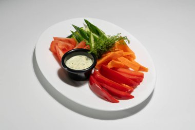 Dilimlenmiş domatesli taze sebze tabağı, salatalıklar, havuçlar ve beyaz arka planda kremalı bitki özlü biberler..