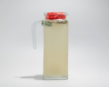 Limonata ve Taze Nane Yapraklı Şeffaf Cam Sürahi Sade Arkaplanda Kırmızı Lid ile Kapalı.