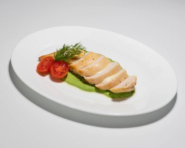 Yeşil püre üzerine dilimlenmiş tavuk göğsü, kiraz domatesli ve beyaz tabakta servis edilen dolma garnitürlü..