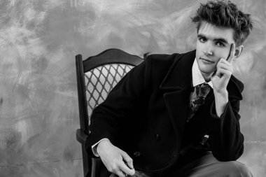 Resmi giyinmiş bir gencin siyah beyaz portresi. Düşünceli bir ifadeyle antika bir sandalyeye yaslanıyor..