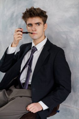 Takım elbiseli genç adam kameraya bakıyor gri arka plan, resmi kıyafet, ciddi ifade.