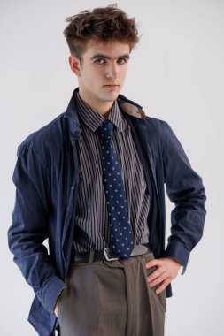 Şık giyinen genç adam beyaz arka planda poz veriyor, çizgili gömlek, mavi kravat ve denizci ceketi giyiyor..