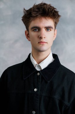 Mavi gözlü ve dağınık kahverengi saçlı bir gencin portresi, gri arka planda beyaz bir gömleğin üzerine siyah bir kadife ceket giyiyor..