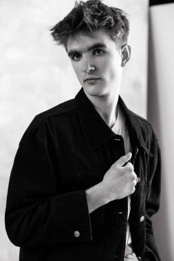 Siyah beyaz bir portre. Kısa, dağınık saçlı, siyah ceketli ve doğrudan kameraya bakan bir genç..