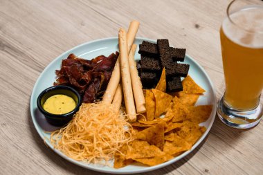 Kurutulmuş et, ekmek, peynir, tortilla cipsi ve bir bardak biranın yanında servis edilen koyu browni de dahil olmak üzere çeşitli atıştırmalıklarla aperatif tabağı..