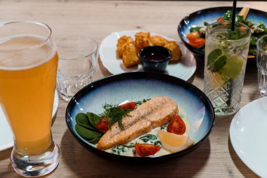 Somon balığı, kızarmış yemek, salata, içecek ve garnitür tabakları ahşap bir masada servis edilir..