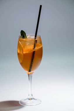 Portakal kokteylini buzla kaplanmış, naneyle süslenmiş ve beyaz arka planda siyah pipetle servis edilen uzun bir bardakta tazeleyici..