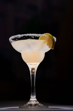 Tuz çerçeveli bardakta klasik margarita kokteyli. Koyu arka planda limon dilimiyle süslenmiş..