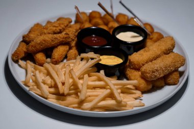 Kızarmış fast food çeşitleri beyaz tabakta soslu, tavuk eti, patates kızartması, mozzarella çubukları ve nugget da dahil..