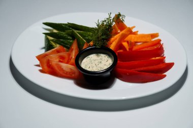 Taze domatesli renkli sebze tabağı, salatalık, havuç, kırmızı biber ve kremalı sos beyaz tabakta servis edilir..