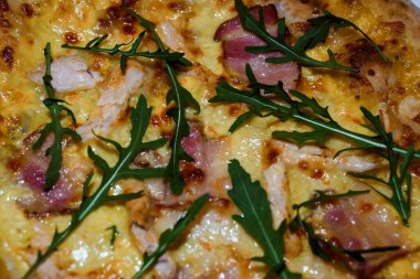 Eritilmiş peynir, prosciutto, tavuk parçaları ve altın kabuklu taze roka yapraklı lezzetli bir gurme pizzanın yakın çekimi..