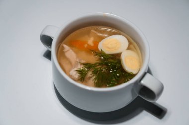 Tavuklu şehriye çorbası, iki parça haşlanmış yumurta ve dereotlu, açık arkaplanda servis edilir..