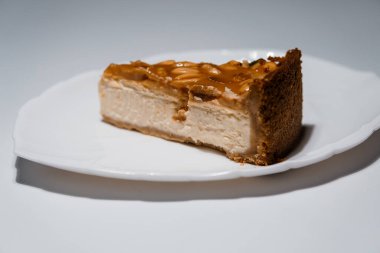 Beyaz bir tabakta fıstık ezmeli lezzetli karamel cheesecake dilimi düz bir arka planda, yakın plan manzaralı..