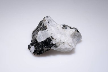 Sade beyaz bir arka plana karşı siyah içerikli ham ay taşı numunesi doğal dokusunu ve parlak parıltısını sergiliyor..
