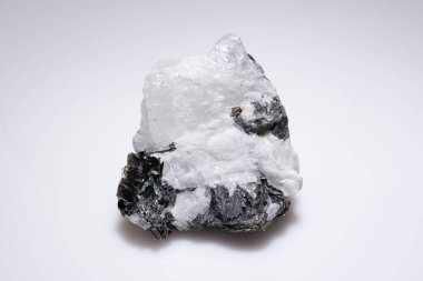 Saf ay taşı kristal numunesi. Sade beyaz bir arkaplana karşı koyu kaplamalı. Doğal şeklini ve ince yanardağını sergiliyor..