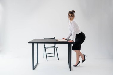 Siyah masaya yaslanan resmi bir kadın, açık bir kitap, beyaz arka plan, profesyonel poz.
