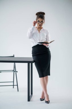 Modern ofis alanındaki masaya yaslanmış kitap okuyan zarif bir iş kadını..