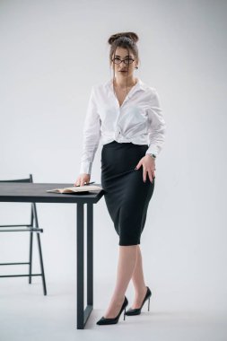 Modern ofis ortamında açık bir kitapla masanın yanında duran kendine güvenen bir iş kadını..
