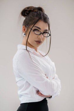 Gözlüklü, kolları çapraz ve ciddi bir ifadeyle kendine güvenen genç bir kadının portresi..