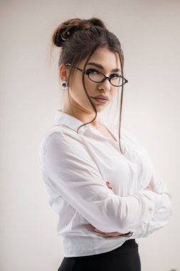 Beyaz gömlekli ve siyah pantolonlu genç bir kadın portresi, kameraya özgüvenle bakıyor..