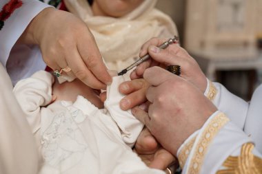 Bir rahibin vaftiz törenini bir bebek üzerinde gerçekleştirdiği, dini tören sırasında küçük bir fırça kullanarak onları İsa yağıyla yağladığı yakın plan bir görüntü..