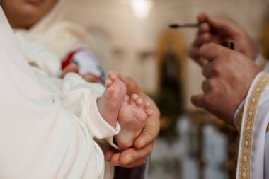 Bir bebeğin vaftiz töreni sırasında bir rahibin bebeğin küçük ayağını kutsal yağ ile kutsadığı, arınmayı ve inanca kabulü simgeleyen hassas bir an..