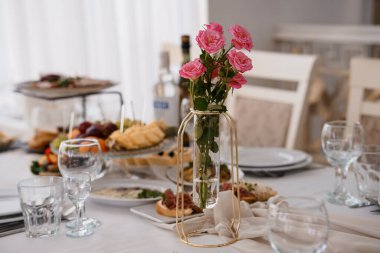 Pembe güller, aperatifler ve şarap kadehlerinden oluşan bir vazo ile şık bir sofra. Parlak ve modern bir yemek odasında kutlama atmosferi yaratıyor..