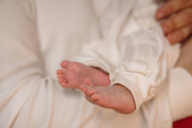 Yeni doğmuş bir bebeğin küçük ayaklarının yumuşak beyaz bir giysi ve yakın bir bağ, bebek, ebeveynlik ve sevgi göstererek nazikçe ailesinin ellerinde tutulacağı hassas bir an..