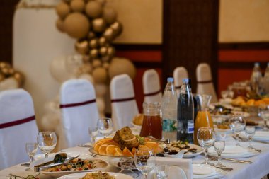 Beyaz çarşaflar, cam örtüler, aperatifli tabaklar ve bir ziyafet salonundaki altın balon süslemeleriyle dolu uzun bir masa..
