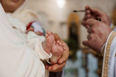 Bir bebeğin Hıristiyan vaftiz töreni sırasında bir rahibin bebeğin ayağını kutsal yağ ile kutsaması, arınmayı ve inançla yeni bir hayatı sembolize etmesi..