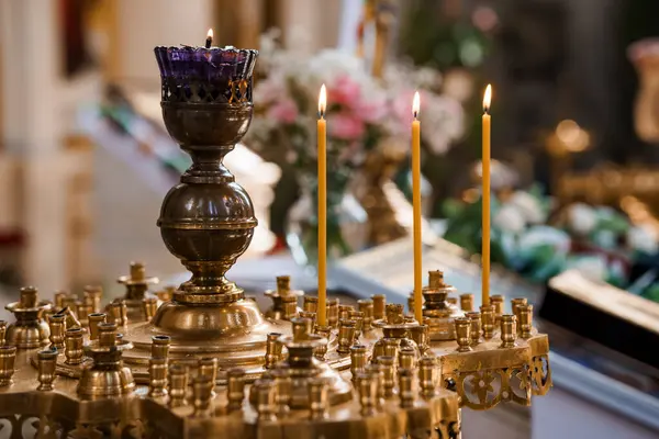 Loş aydınlatılmış bir Ortodoks kilisesinde mumlarla karışık altın şamdanlar, dini adanmışlık, süslü metal eserler ve kutsal bir atmosfer..