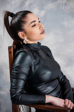 Modern Küpeli ve Sofistike Tarzlı Siyah Deri Giyen Zarif Kadın Özgüvenli İfadesiyle Yanlara Bakıyor.