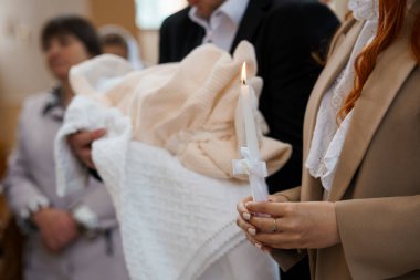 Bulanık bir görüntü Hristiyan vaftiz törenini çekiyor, bir kadın tarafından sarılmış beyaz bir battaniyeye sarılmış bir bebek, etrafında yanan mumlar tutan aile fertleri..