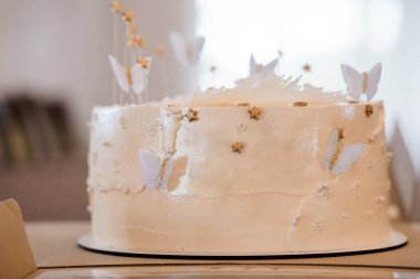Güzel dekore edilmiş üç katlı beyaz bir düğün pastası narin altın yıldızlarla süslenmiş, parıldayan kelebekler, ve dokulu krema, ruhani ve zarif bir tatlı süsü oluşturuyor..