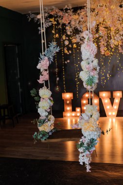 Tavandan sarkan çiçeklerle dolu romantik bir düğün arkaplanı. Büyük bir aşk işareti, sıcak ve büyüleyici bir atmosfer yaratıyor..