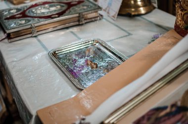 Geleneksel bir Ortodoks kilise ortamında çiçek yapraklarıyla süslenmiş gümüş bir tepside duran alyansların yakın çekimi aşkı, bağlılığı ve maneviyatı simgeliyor..