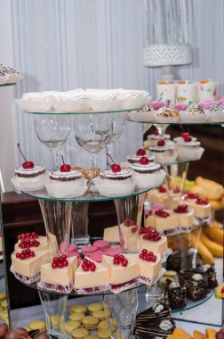 Müsrif bir tatlı masası minyatür kekler, kekler ve meyveli turtalar ile dolup taşar, katmanlı cam standlarda güzelce düzenlenir, zarif ve davetkar bir şekerleme üretir.