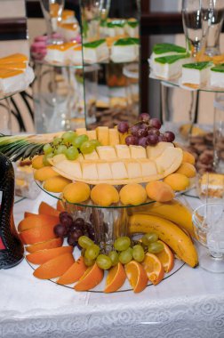 Karpuz, üzüm, portakal, muz ve hamur işleri gibi taze meyvelerin sergilendiği zarif bir düğün tatlı masası, beyaz çarşaflarda sergileniyor..